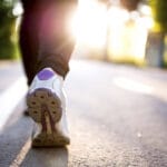 Close-up of a person walking on a paved path outdoors in athletic shoes, with sunlight shining—perfect for sparking exercise motivation.